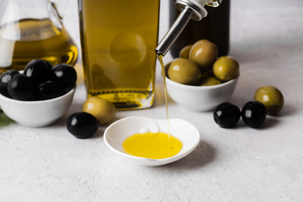 Olio d'oliva versato in ciotola, olive verdi e nere.