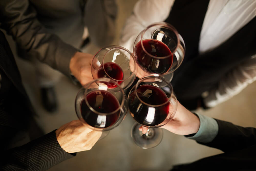 Quattro persone brindano con calici di vino rosso.