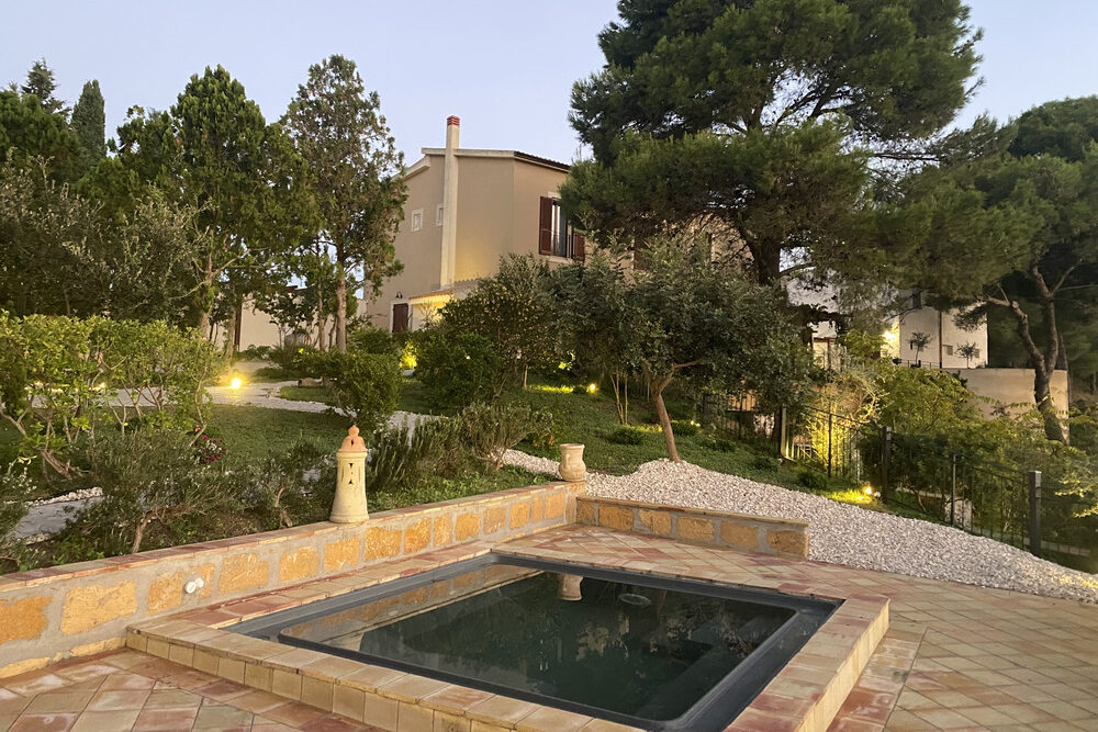 Mini piscina illuminata, giardino e villa sullo sfondo.